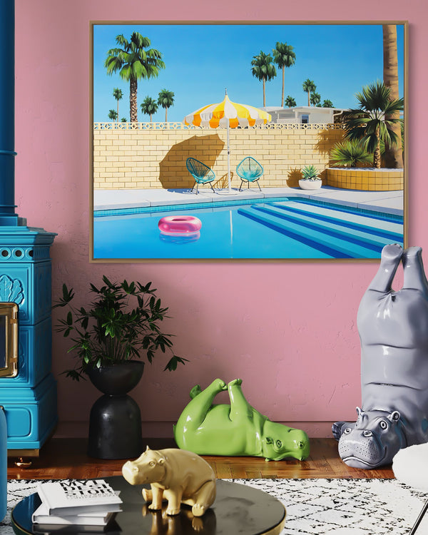 A yellow and white striped umbrella provides shade over a pink pool ring floating in a crystal clear swimming pool on a sunny summer day in Palm Springs.