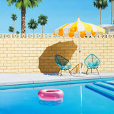 A picturesque swimming pool scene featuring a whimsical pink pool ring and a sunny yellow and white striped umbrella on a summer day in Palm Springs.