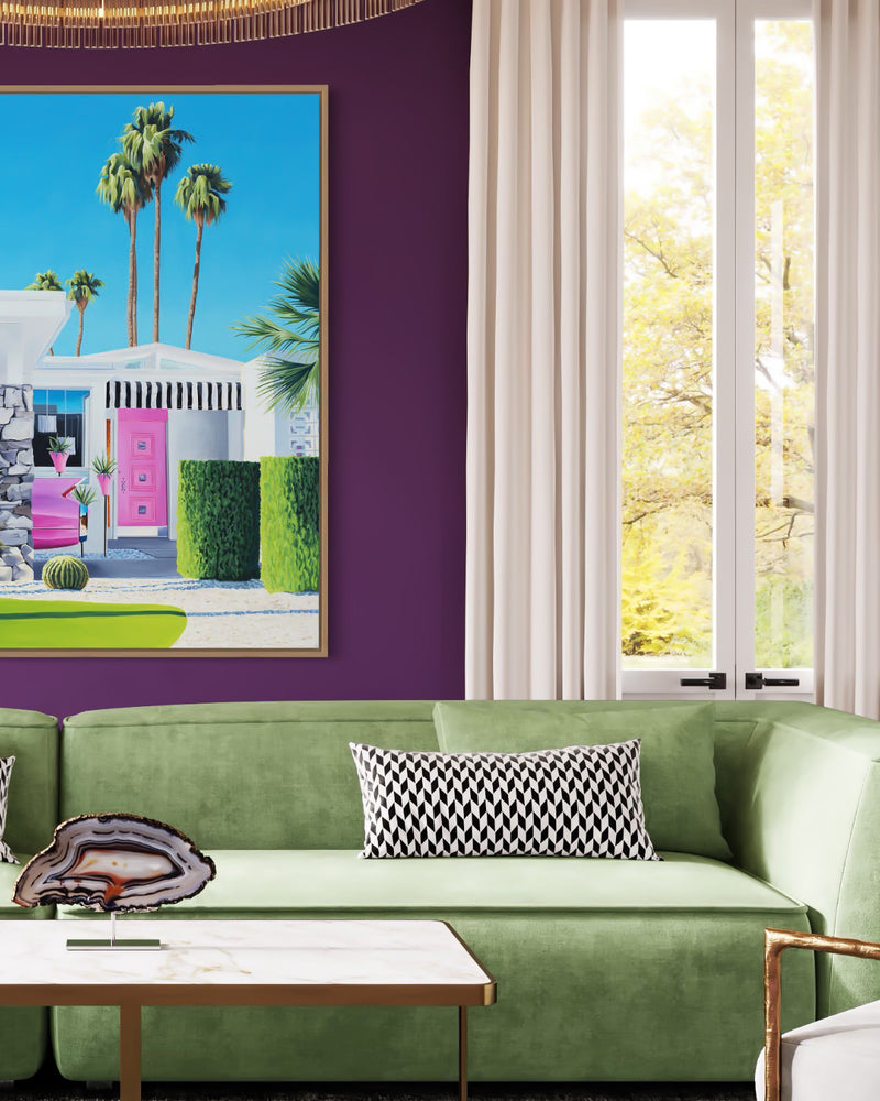 A beautiful piece of art in a chic living room. The painting features midcentury architecture and a pink Cadillac, adding a pop of color. Relaxing palm trees complete the scene